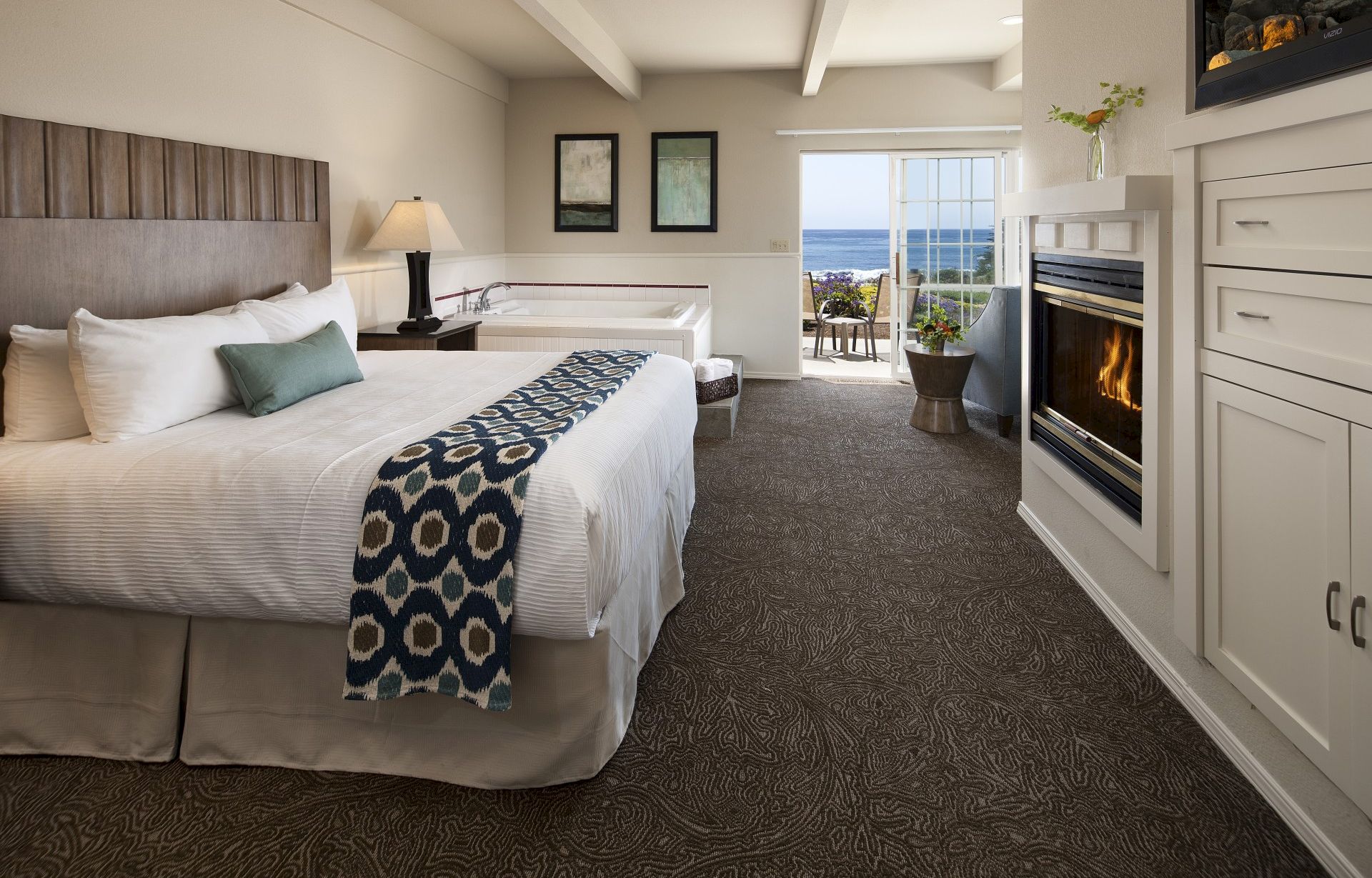 A modern hotel room with two large beds, a fireplace, a cozy seating area by a window, and a soft neutral color palette.