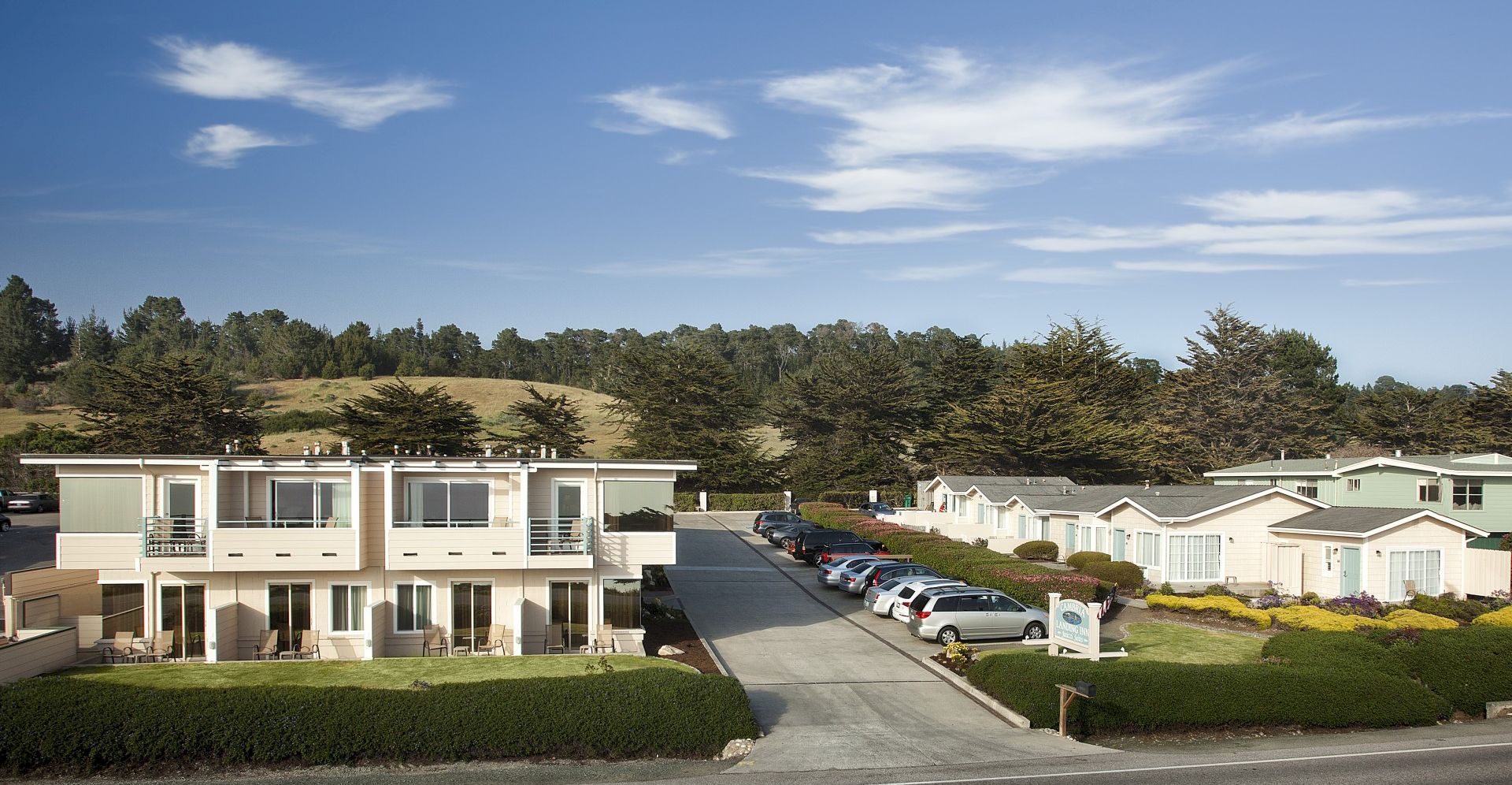Residential apartments and mobile homes in a suburban cul-de-sac, with a paved road, parked cars, and green landscaping under a blue sky.
