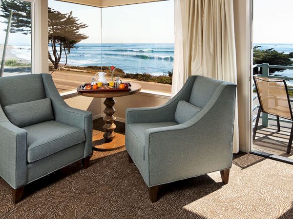 Cozy beachfront lounge with two blue armchairs, a small round table, and a view of the ocean through large windows. Enduring calm.