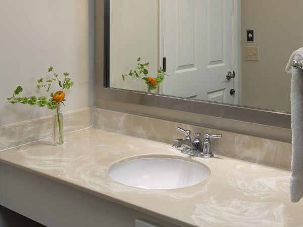 A bathroom sink with a marble countertop, a mirror above, a small vase with flowers, and a towel hanging on the right.
